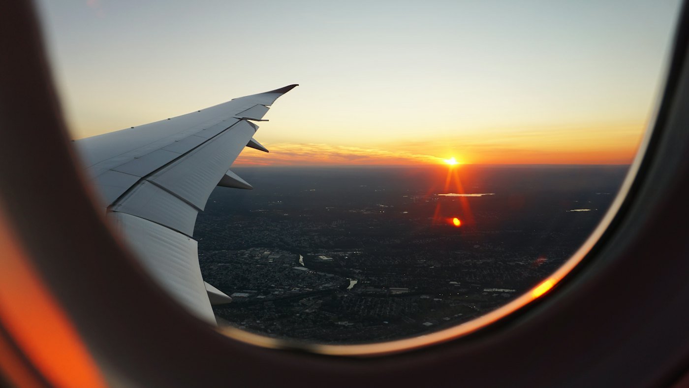 Asa do avião vista pela janela do passageiro, com o sol no horizonte